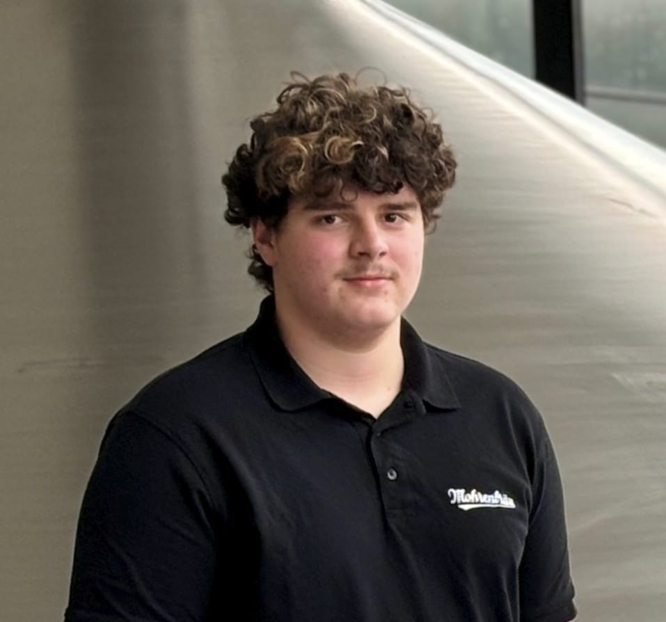 Young man with curly brown hair in black polo shirt.