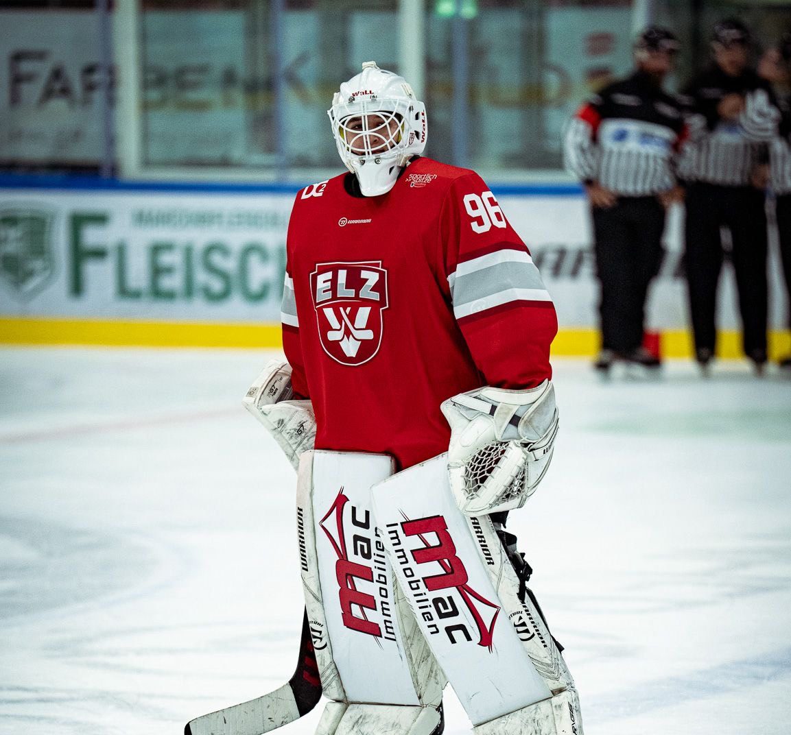 Ice hockey goalie in red jersey with number 96 on ice rink, looking forward.