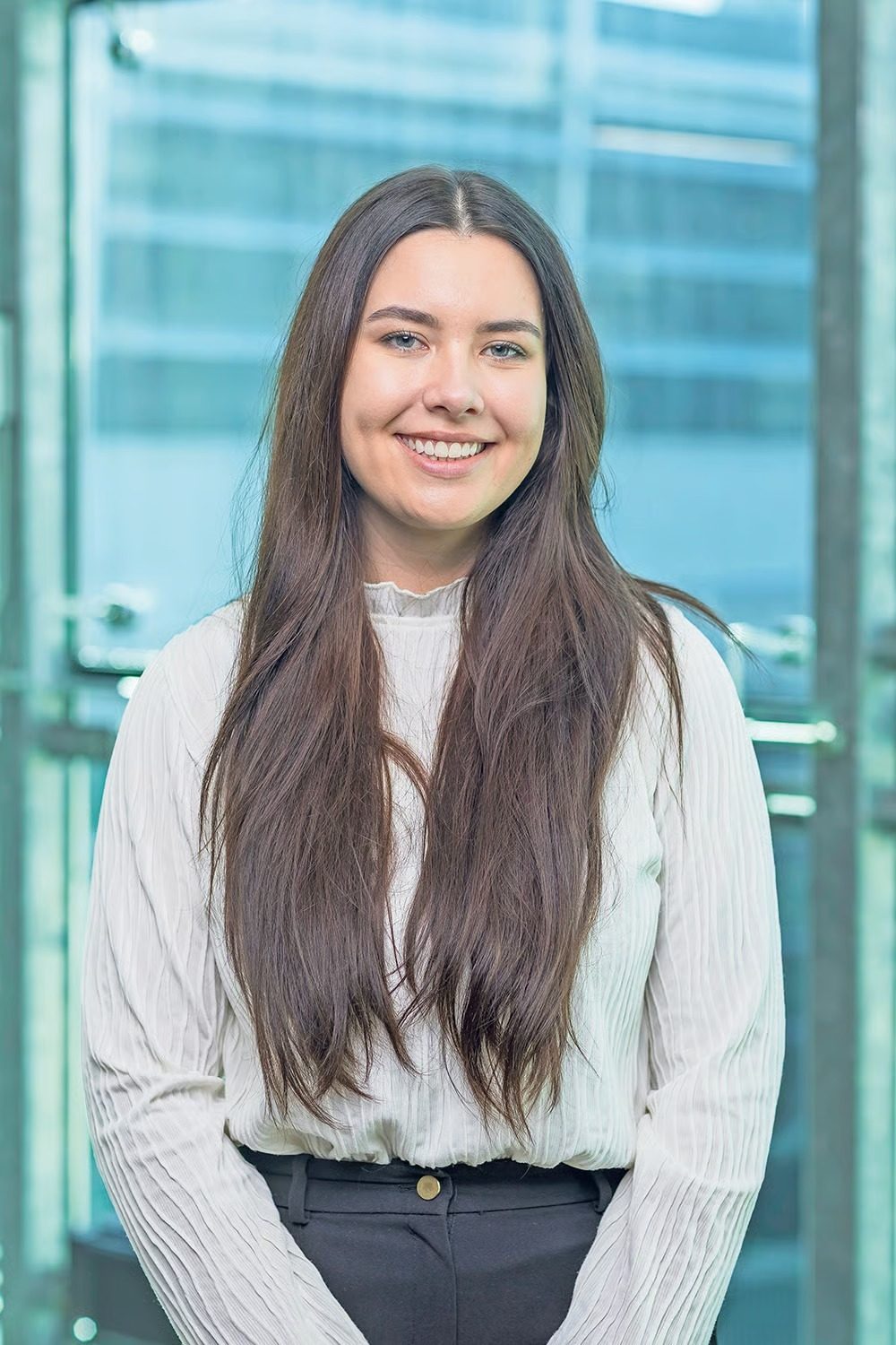 Smiling woman with long dark hair, white shirt, blue background.