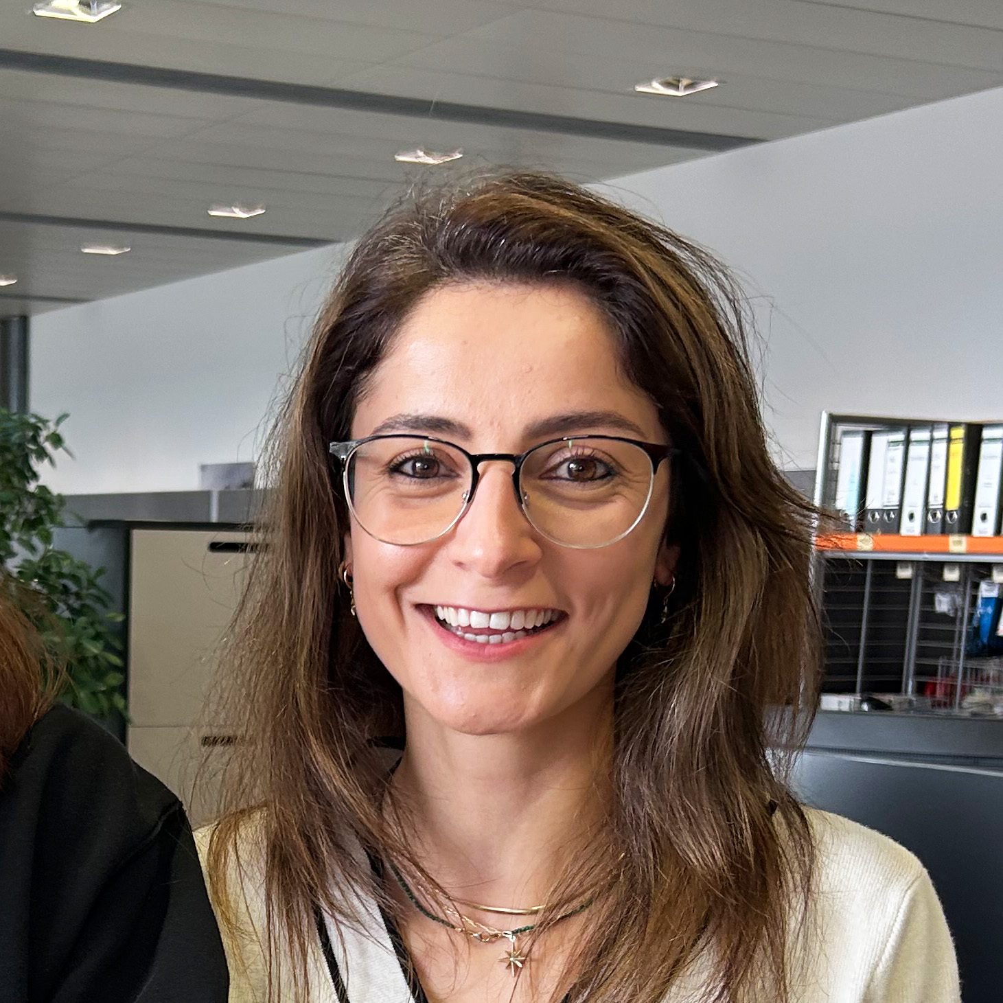 A smiling woman with brown hair and glasses in an office setting.