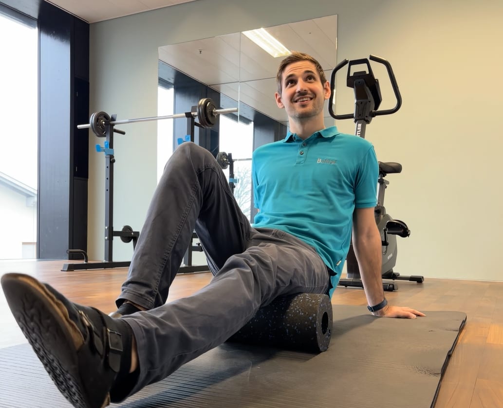 Smiling man foam rolling on a mat in a gym.