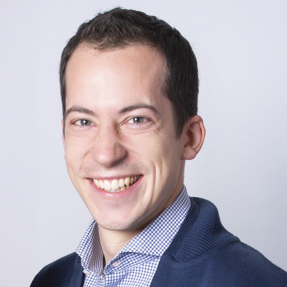 Smiling man in blue checkered shirt and cardigan.