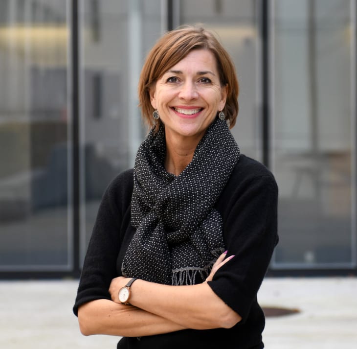 Smiling woman with short brown hair, black top, patterned scarf, and arms crossed.
