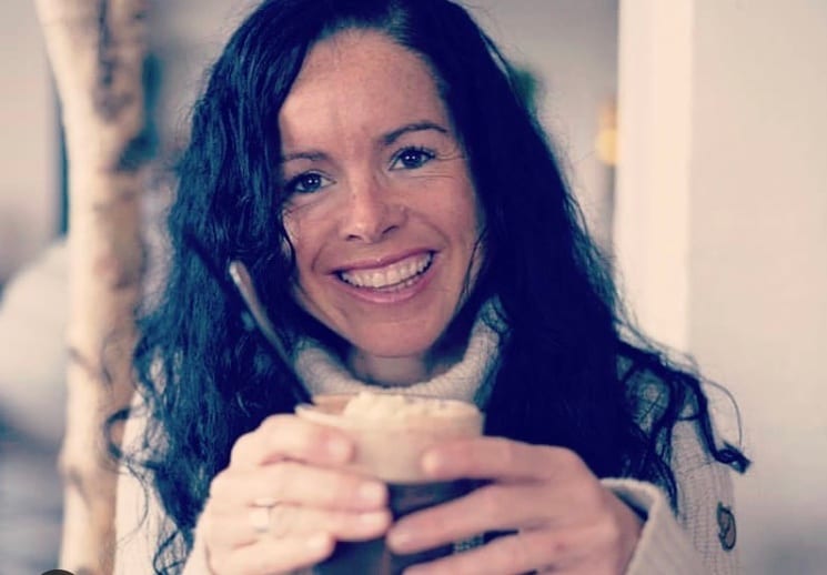 Smiling woman in a turtleneck holding a frothy drink.