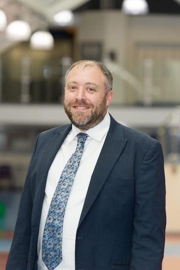 Dress shirt, Facial hair, Chin, Smile, Beard, Sleeve, Coat, Tie, Grey, Collar