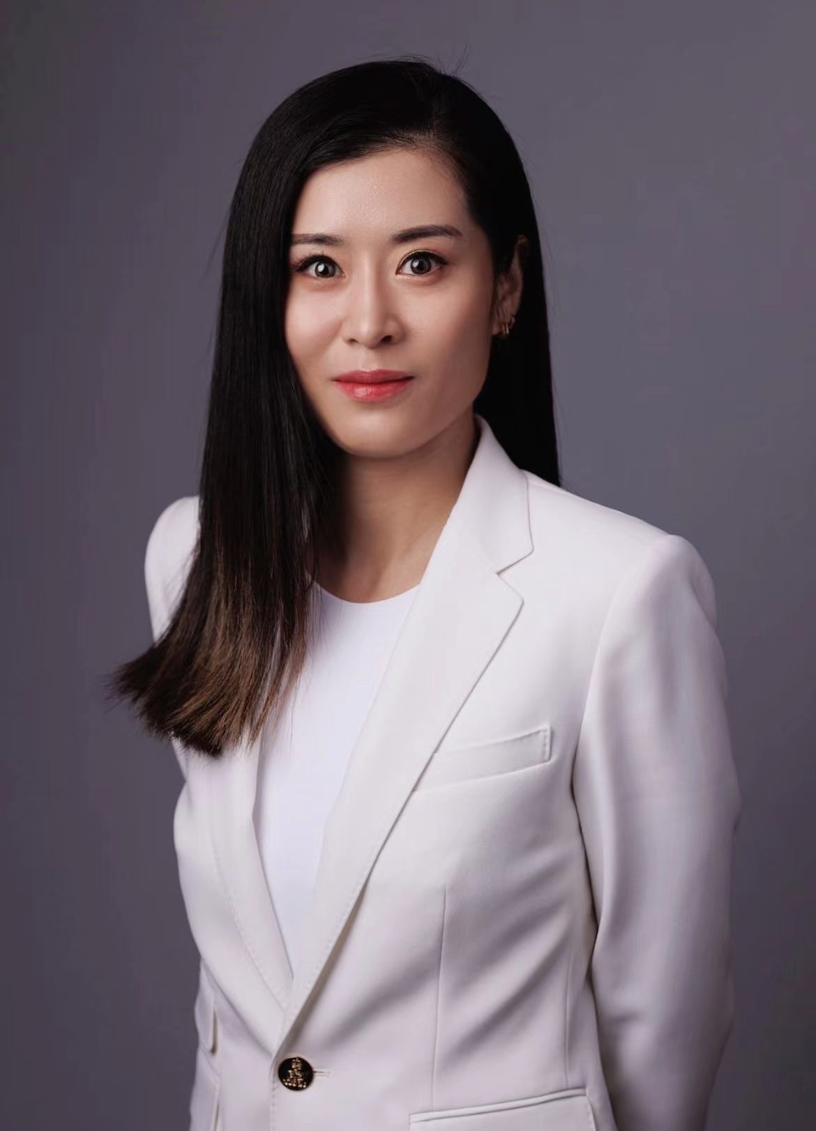Woman in white blazer with long dark hair against a gray background.