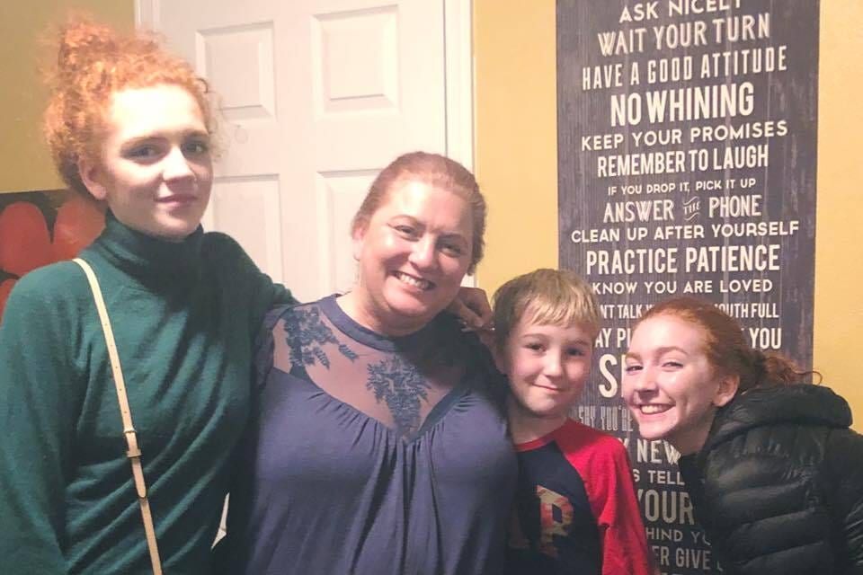 A family of four, including two red-haired girls, a boy, and a woman, smiling for a photo indoors.