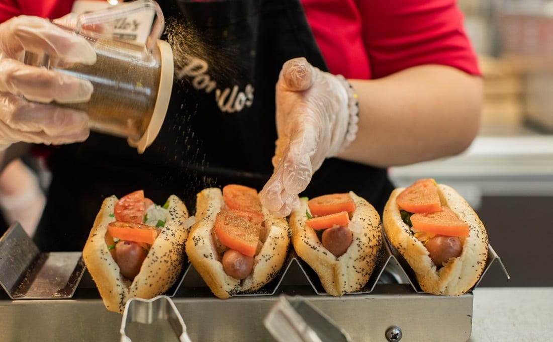 Employee applying toppings to four hot dogs
