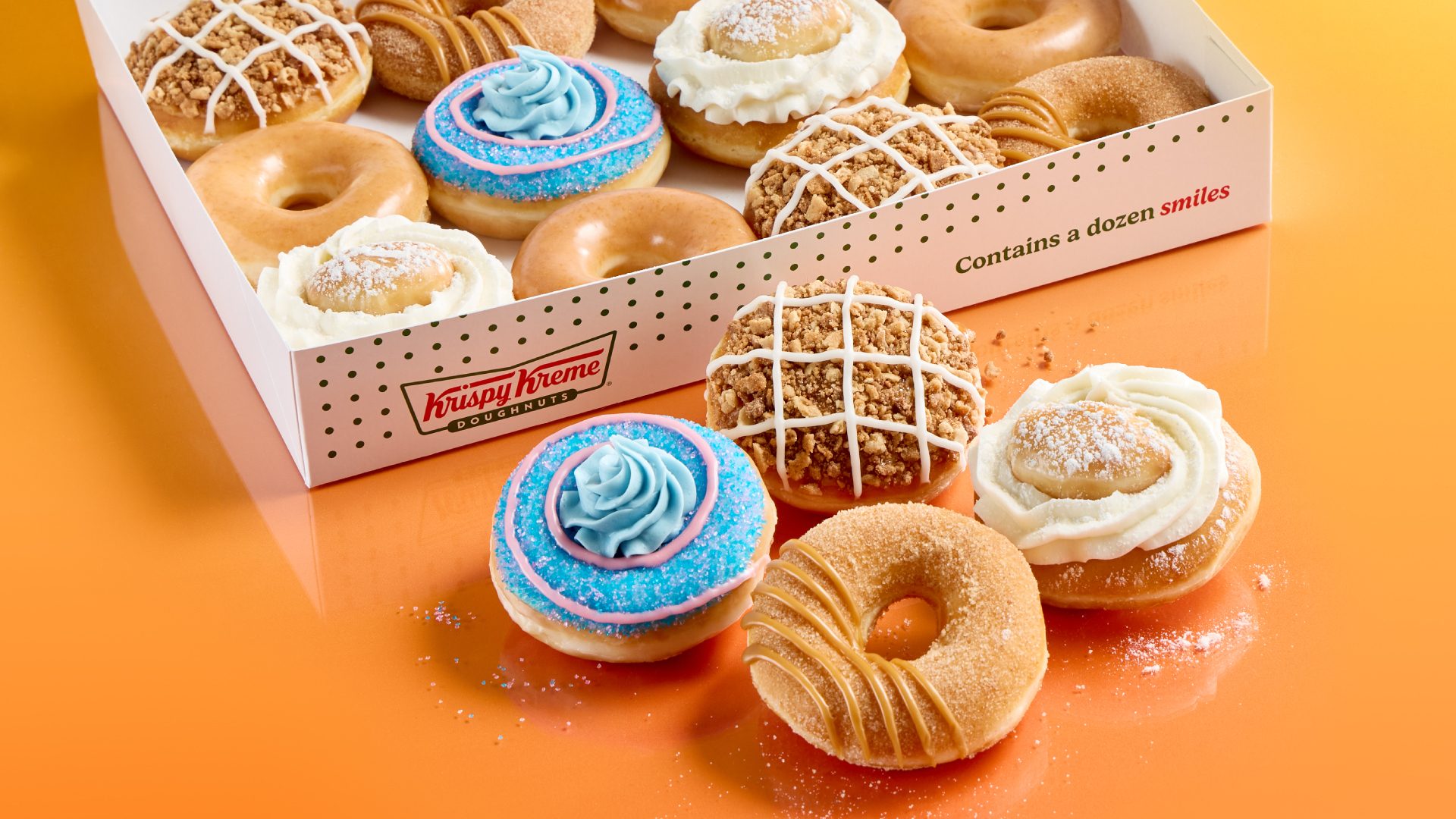 Krispy Kreme box of diverse donuts, some outside, on a bright orange surface.