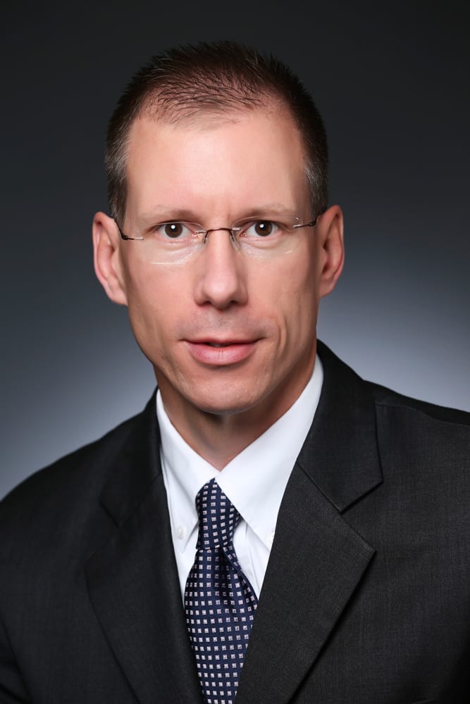 Headshot of a man in a suit, tie, and glasses.