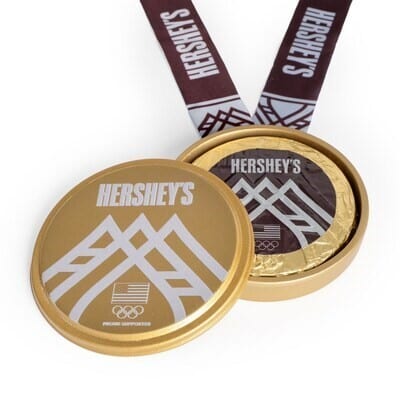 A Hershey's chocolate medal with a gold case and ribbon, featuring Olympic-themed designs.