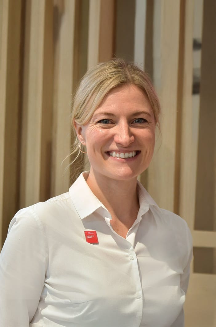 Smiling woman in a white shirt, wearing a red name tag.