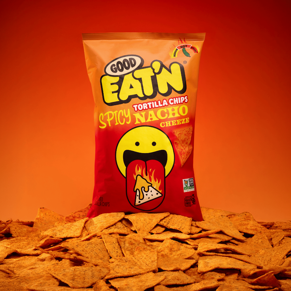 Bag of Good Eat'n Spicy Nacho Cheeze Tortilla Chips on a pile of chips against an orange background.