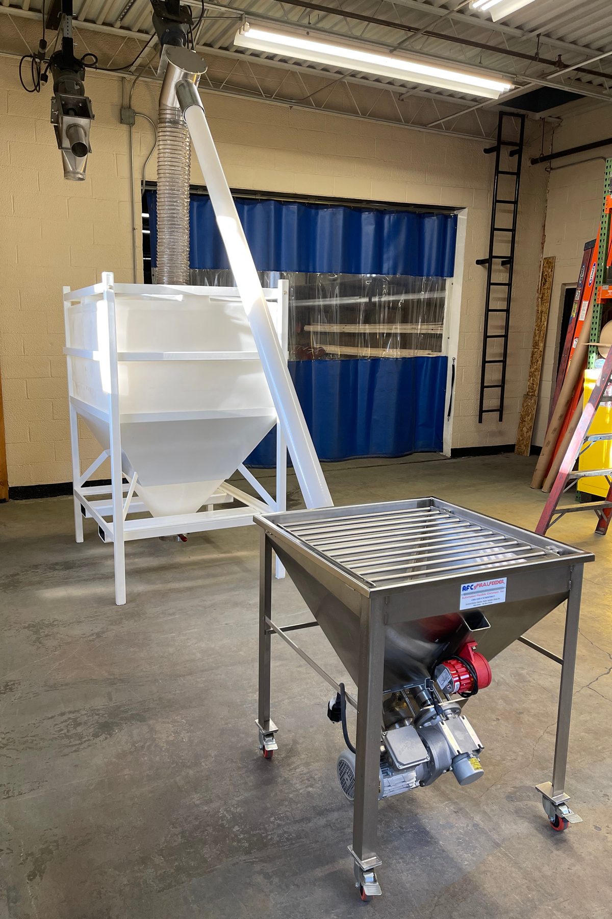 White material hopper, stainless spiral feeder with motor, and conveyor tube in industrial setting.