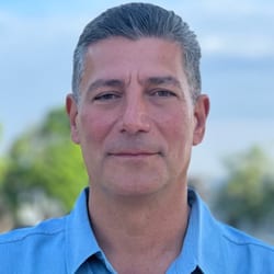 Headshot of a man with grey hair in a blue shirt, looking directly at the camera.