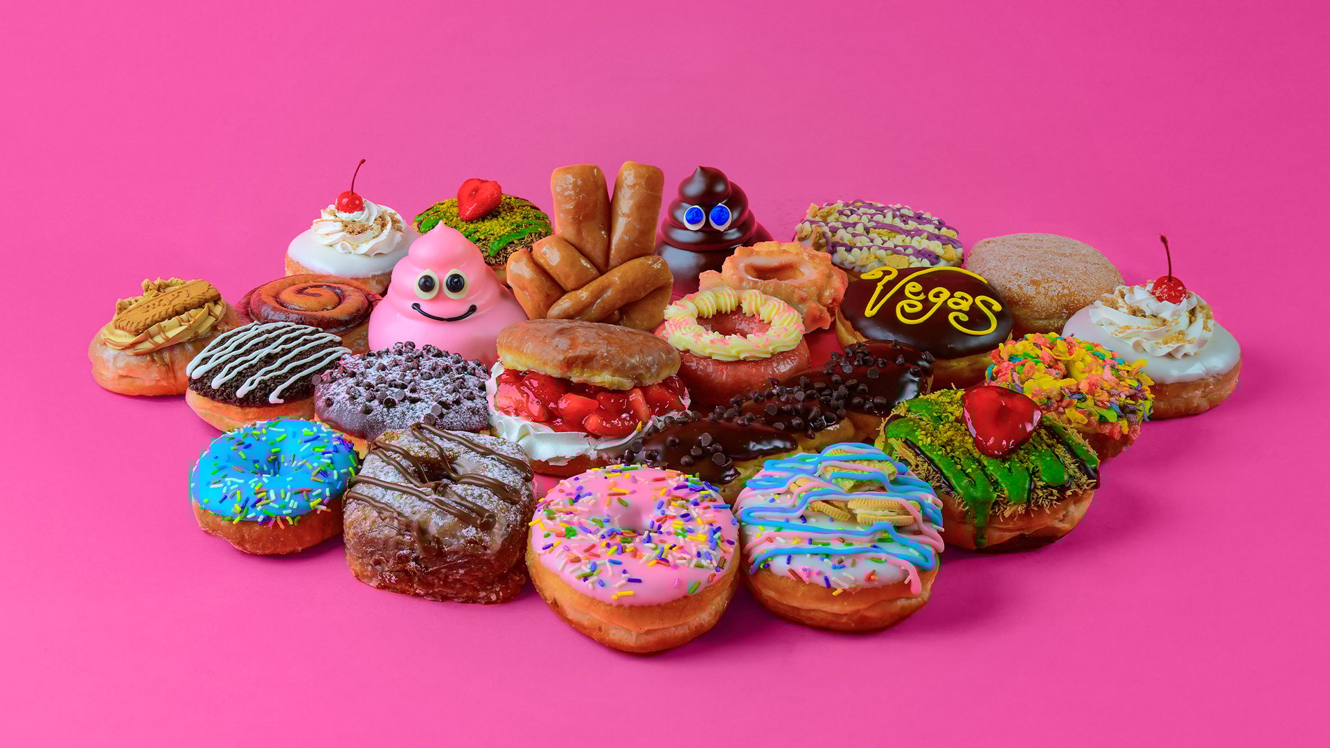An array of uniquely decorated, colorful donuts on a bright pink surface.