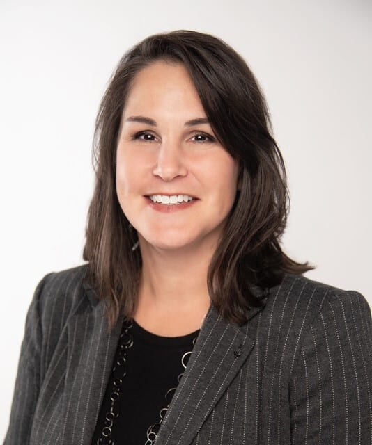 Headshot of a smiling woman with dark hair in a pinstripe blazer, looking directly at the viewer.