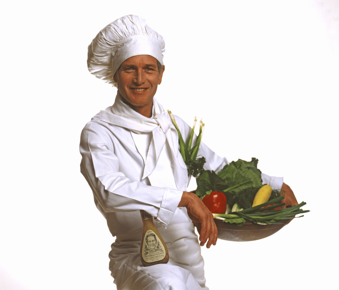 Paul Newman as a smiling chef, holding vegetables and Newman's Own dressing.