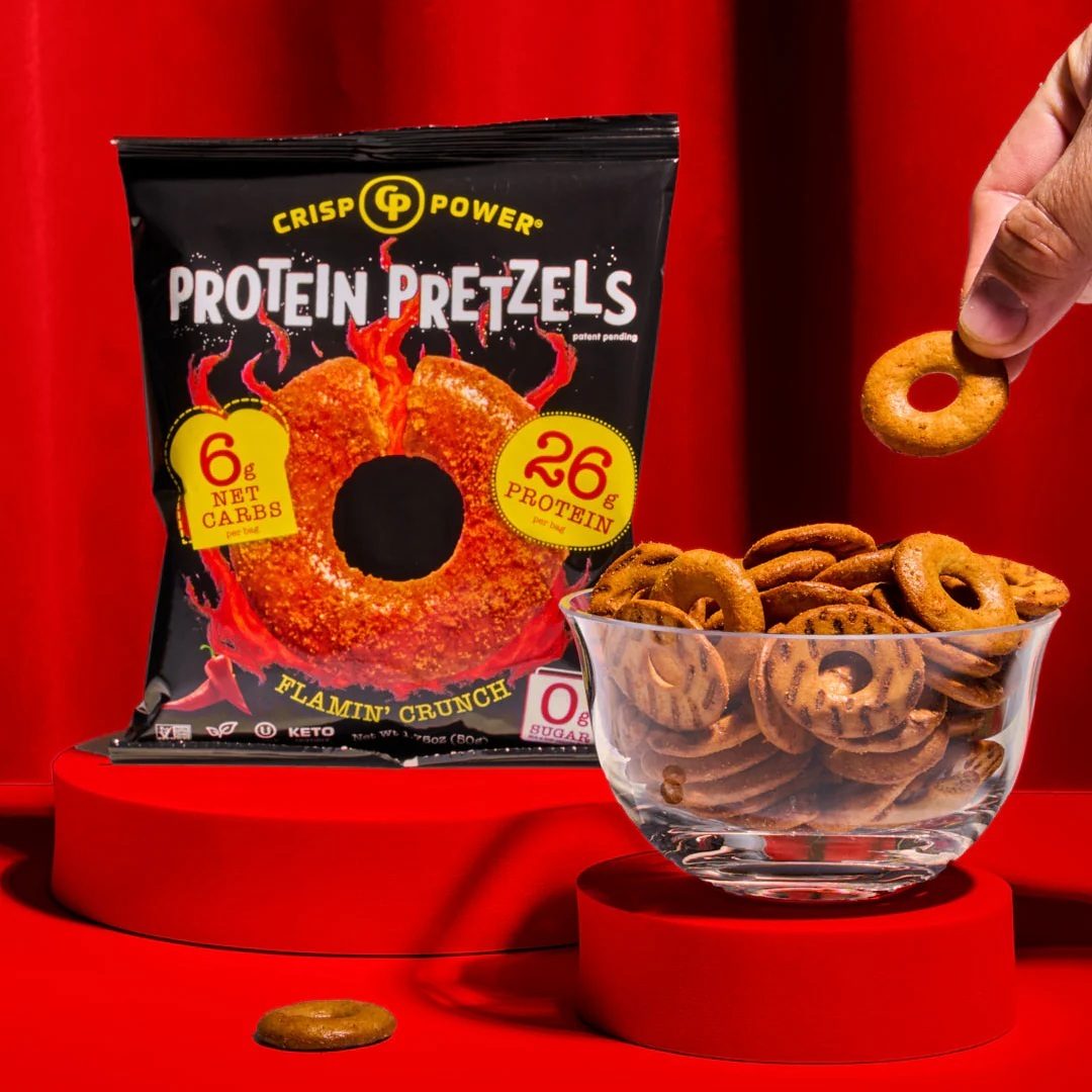 Crisp Power Protein Pretzels bag, bowl of pretzels, and a hand holding one, all on red platforms.