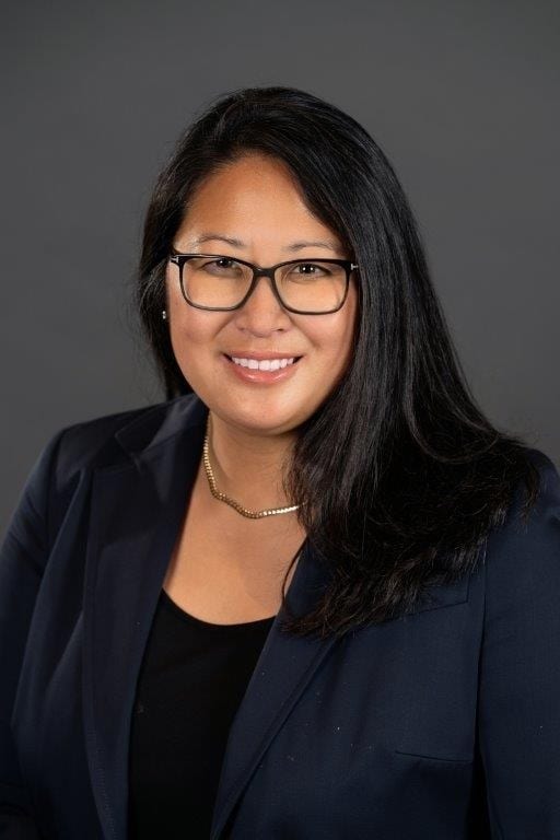 Smiling Asian woman with glasses, long dark hair, and a dark blazer.