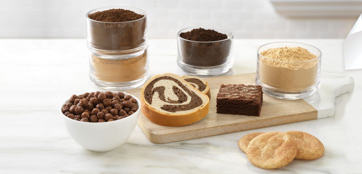 Jars of powders, chocolate cereal, marble bread, brownie, and snickerdoodle cookies on a board.