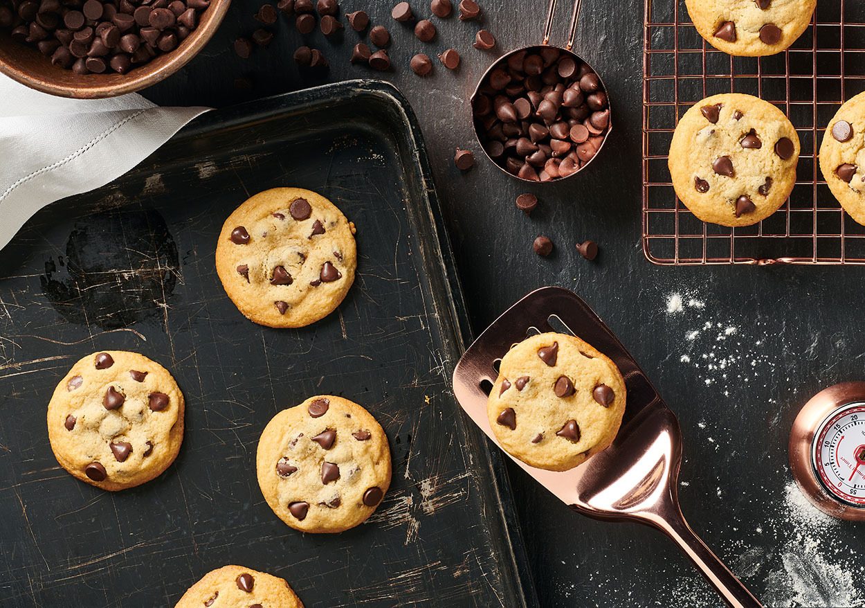 Chocolate chip cookies on a baking sheet, wire rack, and spatula