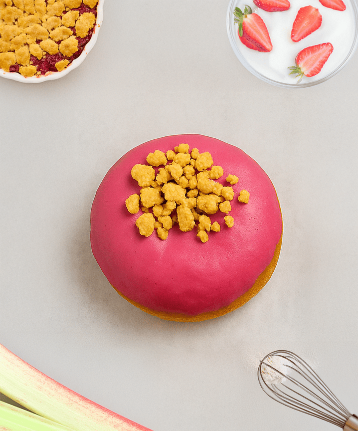 Pink donut with crumbs, rhubarb crumble, yogurt with strawberries, rhubarb, and a whisk.
