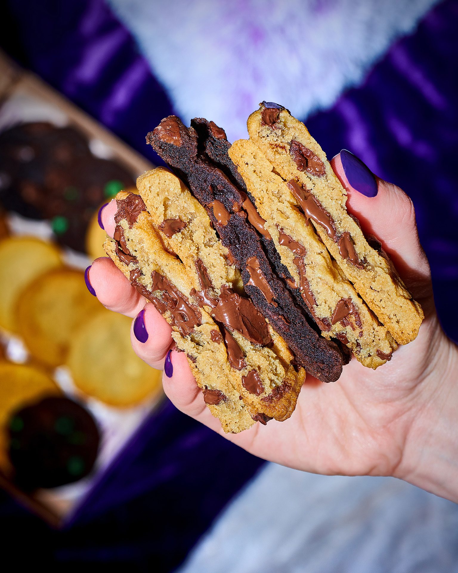Hand with purple nails holding split chocolate chip and double chocolate cookies with melted chocolate.