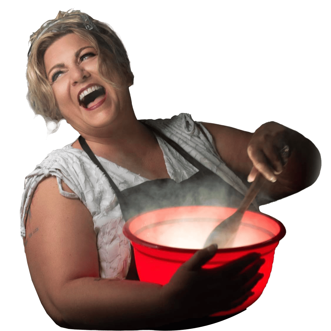 A laughing woman in an apron stirring a glowing red bowl with a spoon, steam rising from the contents.
