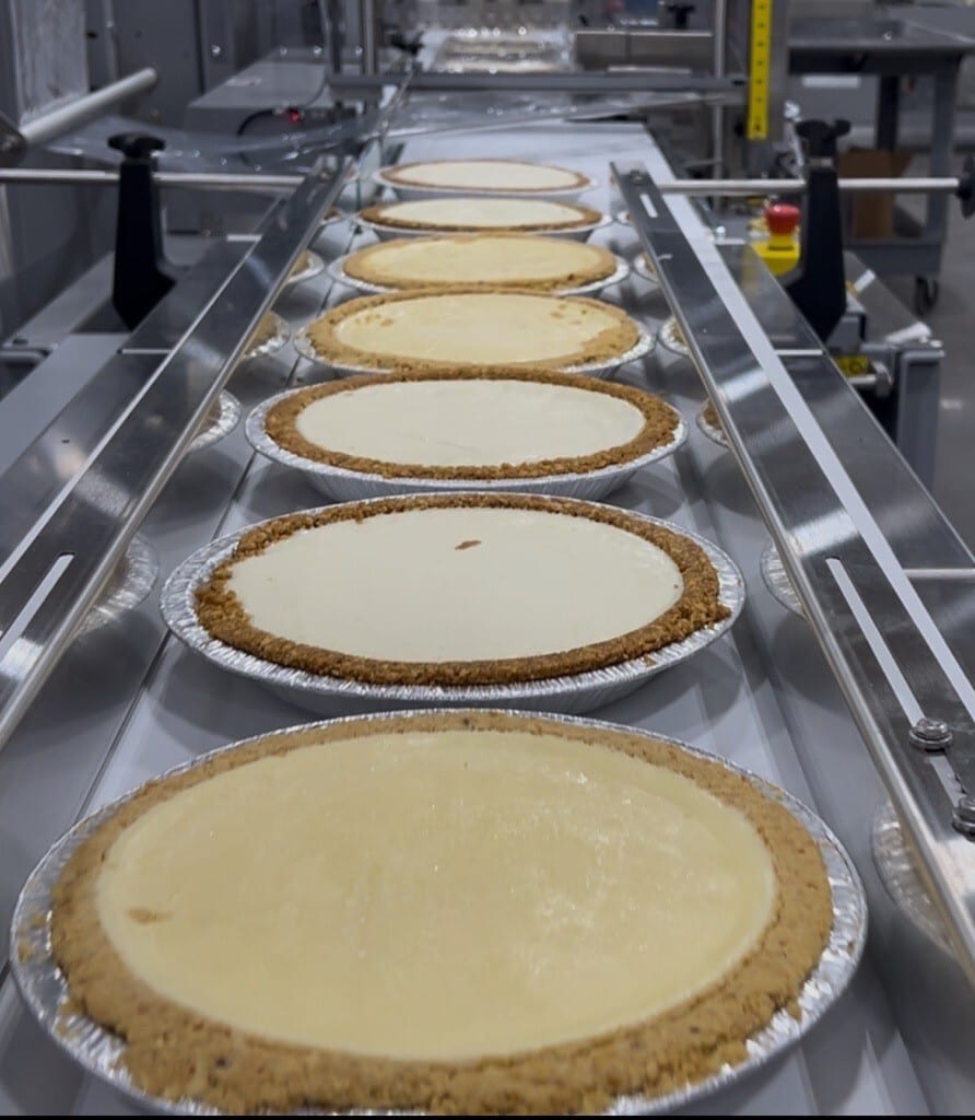 Cheesecakes with graham cracker crusts on a factory conveyor belt.