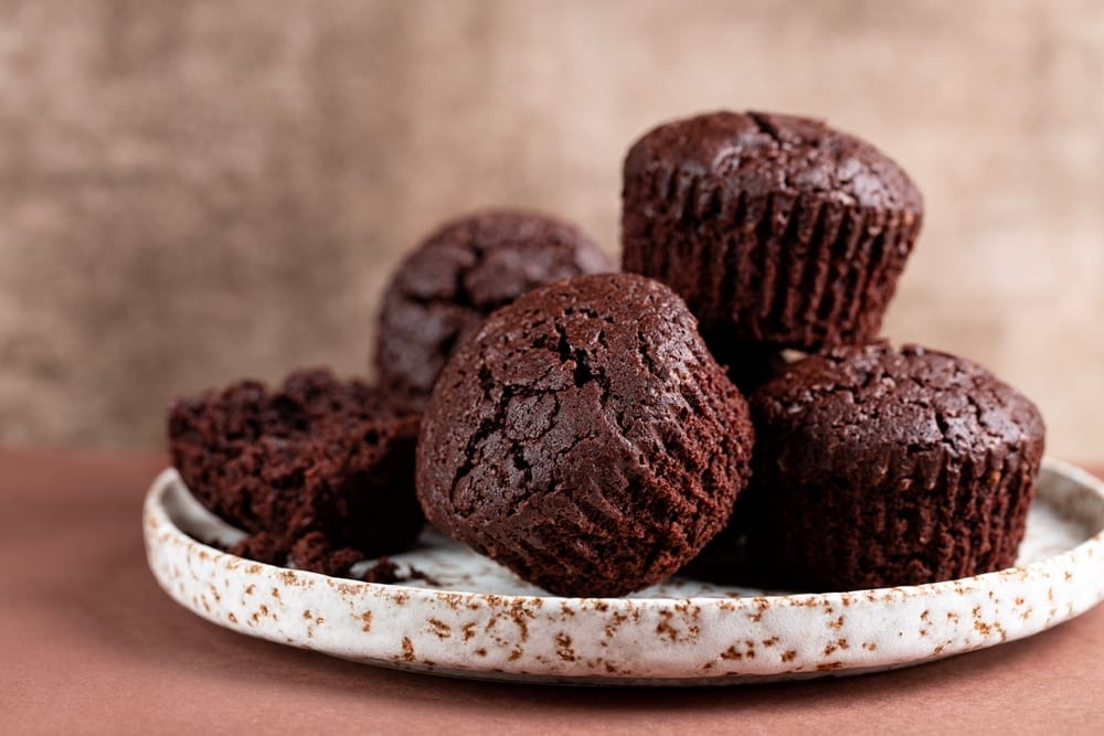 Chocolate muffins piled on a speckled white plate, one broken open.