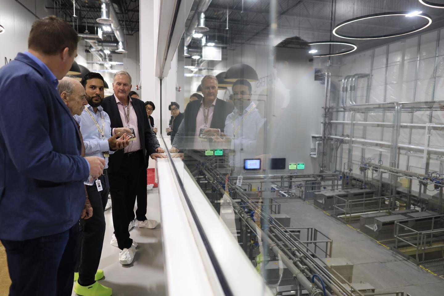 People observe a clean industrial facility through a glass partition.