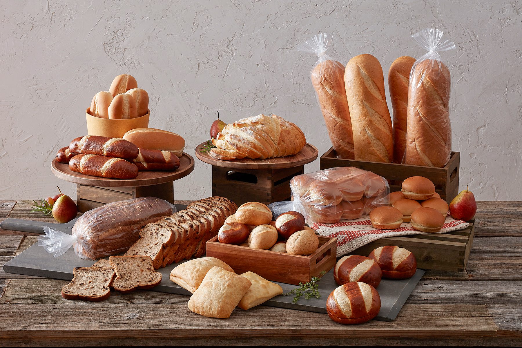 Diverse fresh breads and rolls, some bagged, arranged on wooden stands and boards.