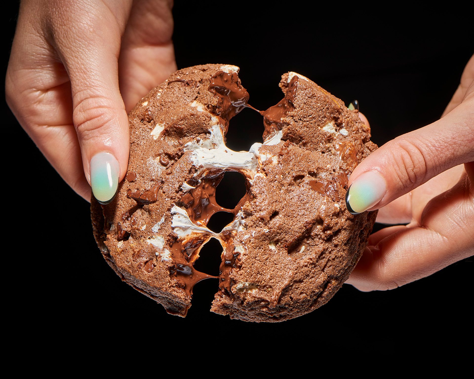 Hands pulling apart a gooey chocolate marshmallow cookie.