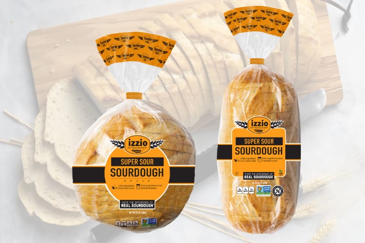 Two clear bags of Izzo Super Sour Sourdough bread, one round and one oblong, on a wooden board.