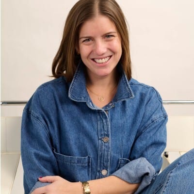 A smiling woman with brown hair, wearing a denim jacket and a gold necklace.