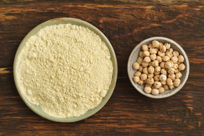 Large plate of chickpea flour next to smaller bowl of chickpeas