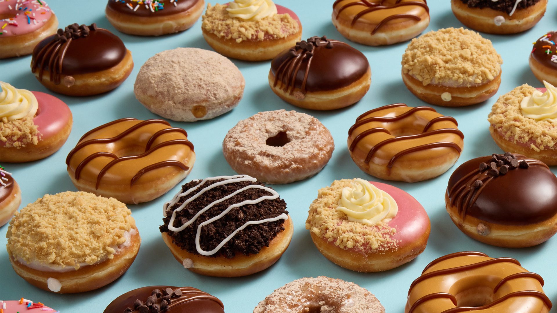 Many different donuts with various frostings and toppings on a blue background.