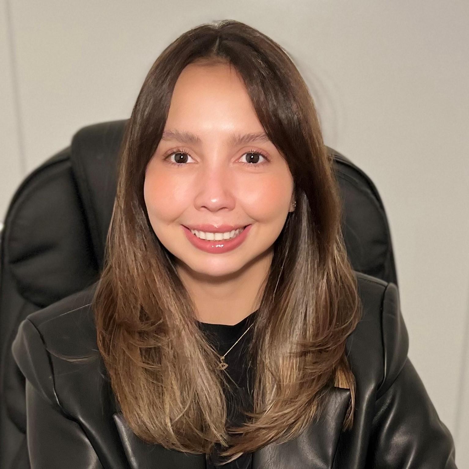 Smiling woman with long brown hair in a black leather jacket.