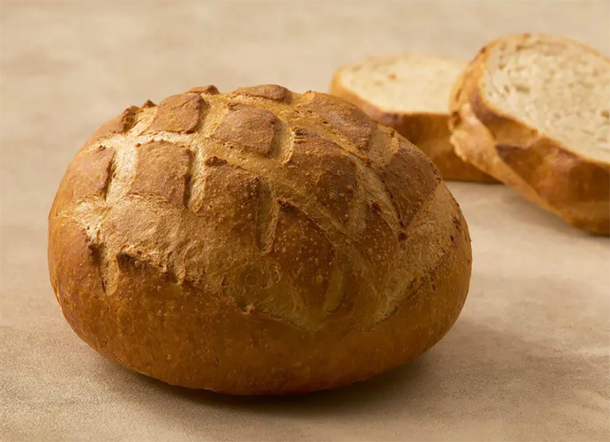 Golden-brown round bread loaf with a scored crust, and two blurred slices in the background.