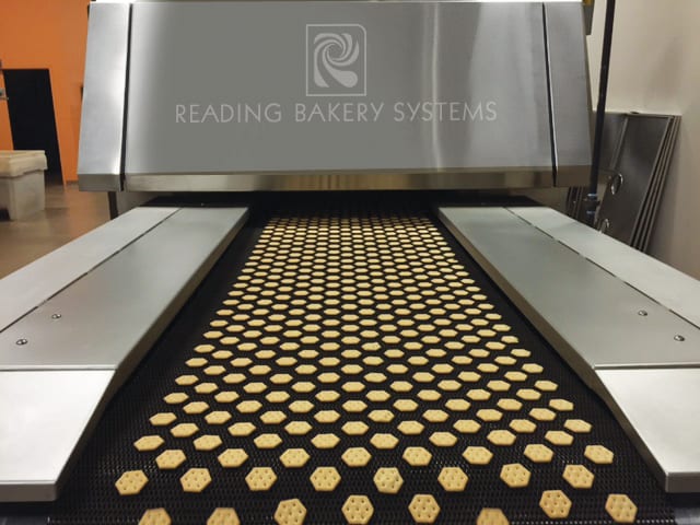 Hexagonal crackers on a conveyor belt entering a Reading Bakery Systems machine.