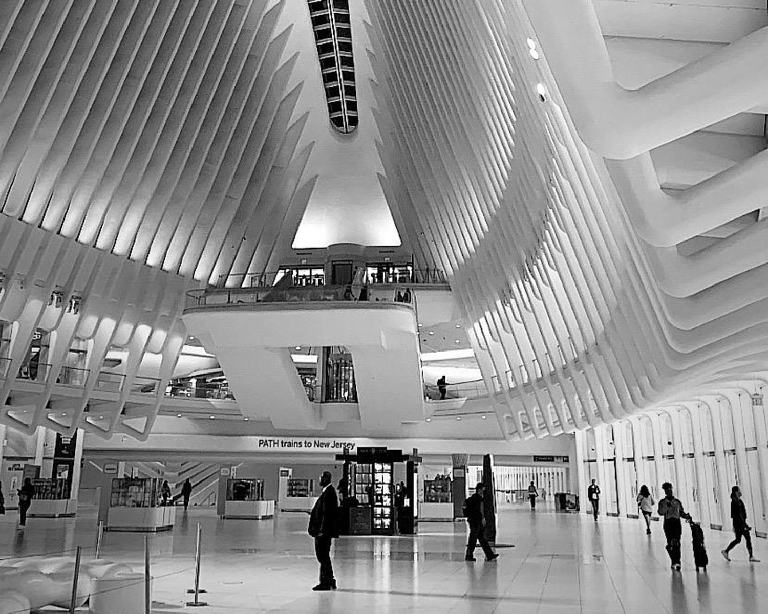 B&W photo of a modern, white-ribbed train station interior with people.