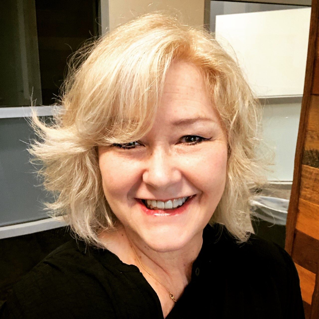 Smiling woman with short blonde hair, black top, and gold necklace.