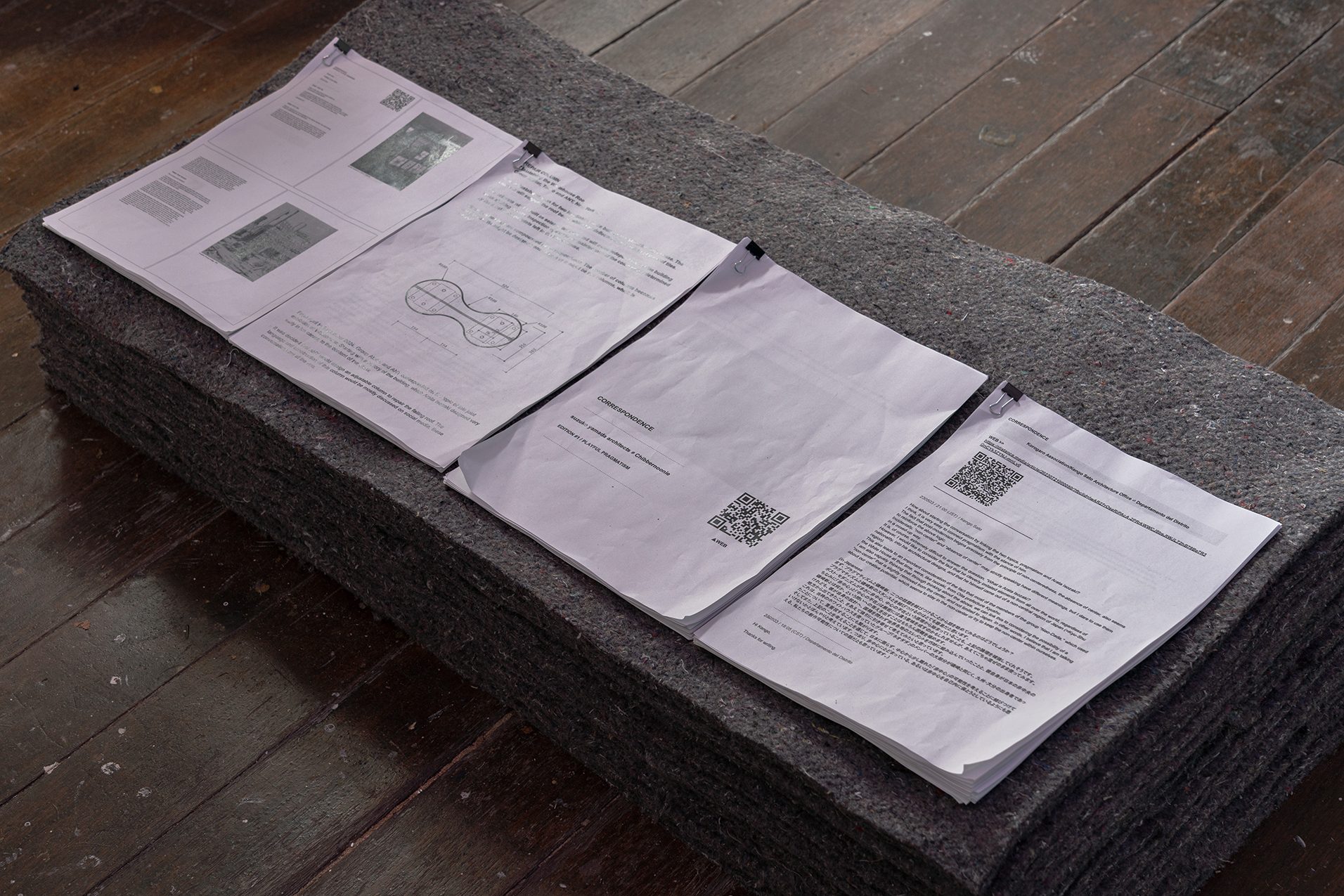 Stacks of white papers with architectural text and diagrams, on gray felt, over a wooden floor.