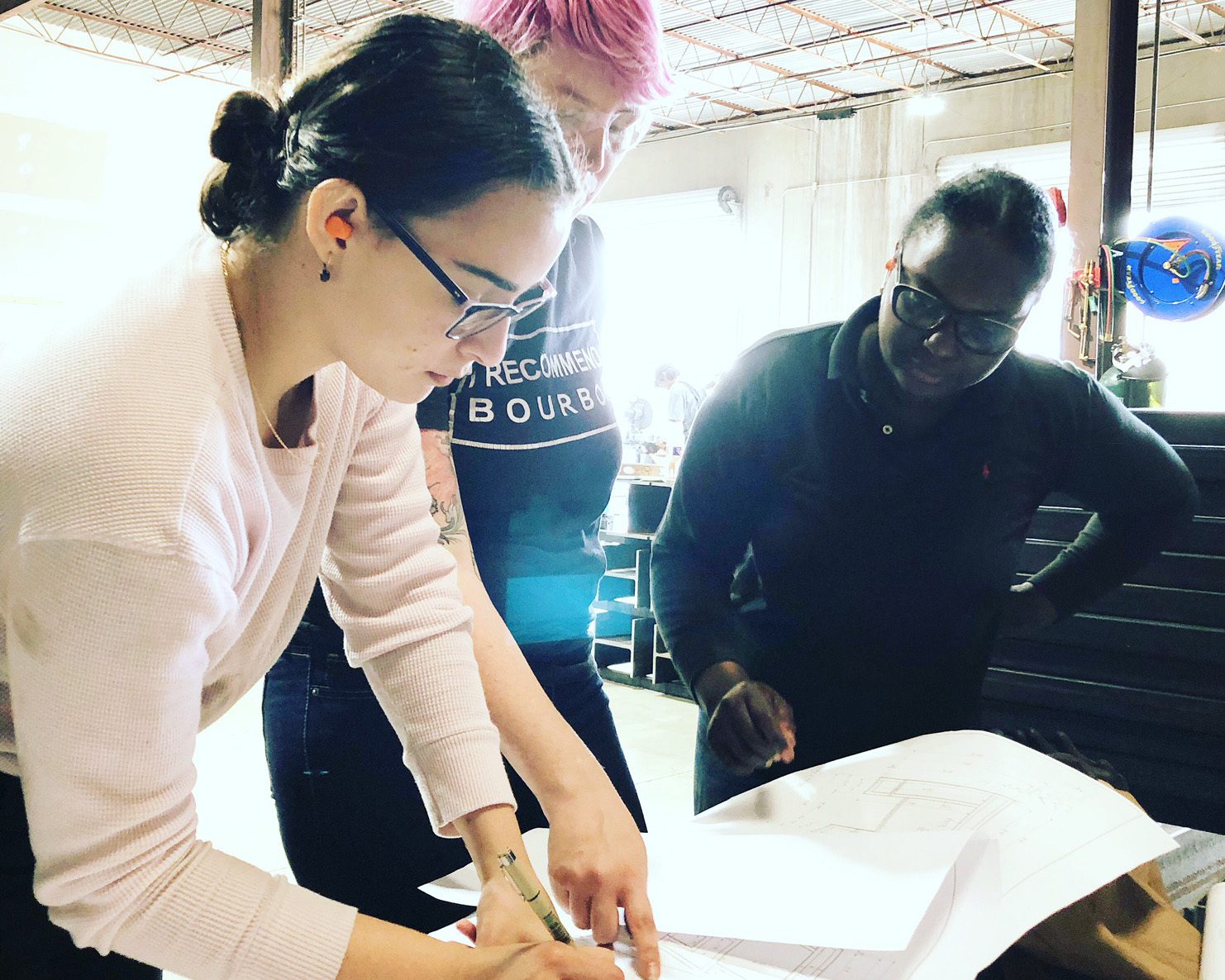 Three people, two women and one man, collaboratively reviewing blueprints in a workshop.