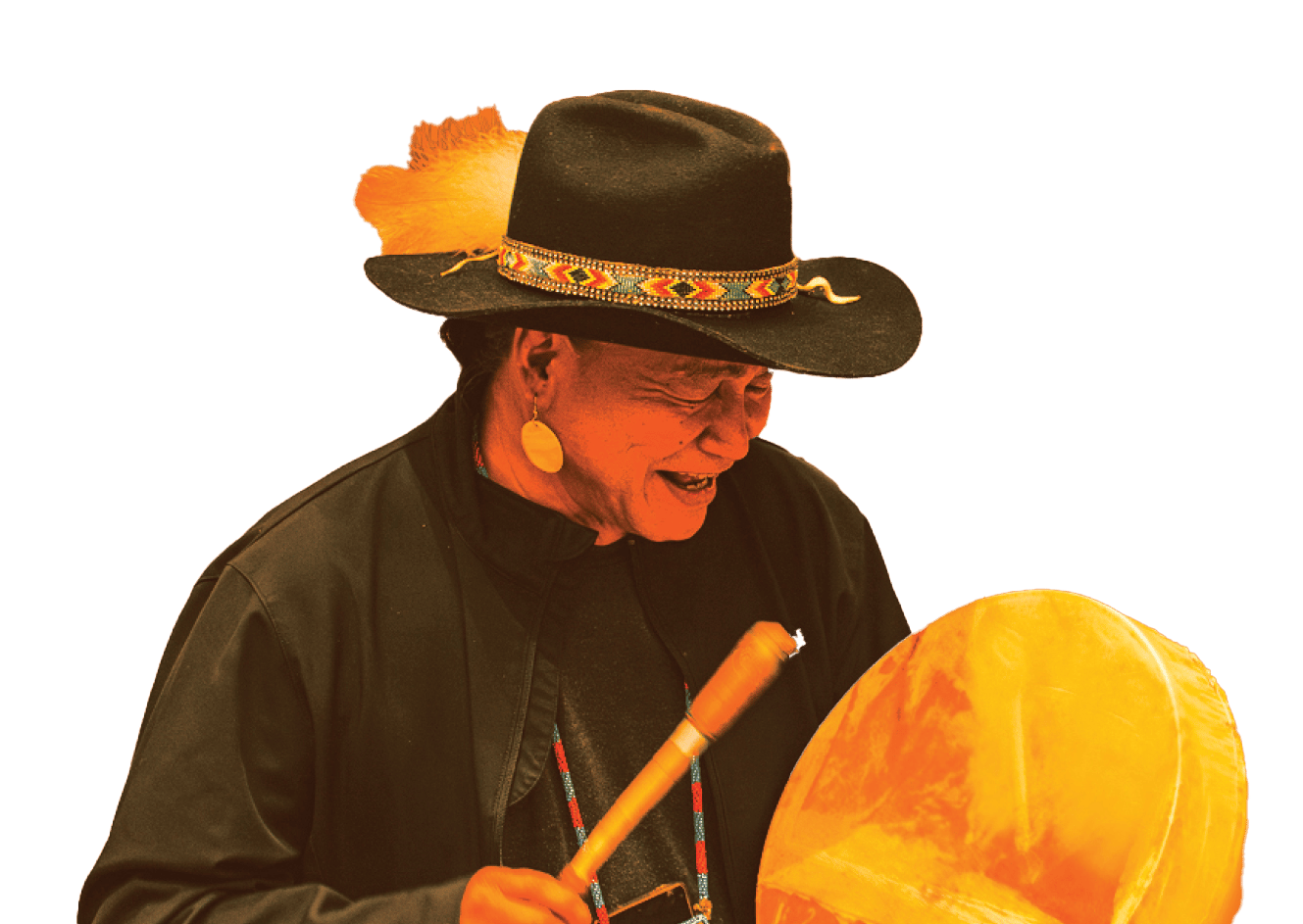Indigenous person in hat with feathers and beads, smiling, playing a large drum with a drumstick.