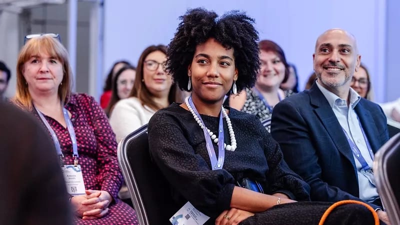 Three diverse people, including two women and a man, attending a conference with smiles.