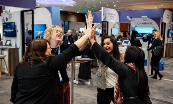 Four women high-fiving and laughing at an event booth.