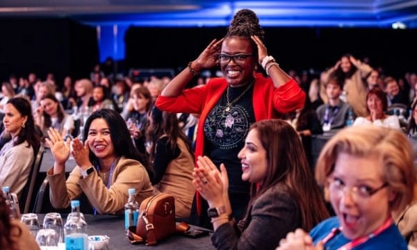 Diverse women attendees at a conference, some clapping and smiling, showing excitement and engagement.