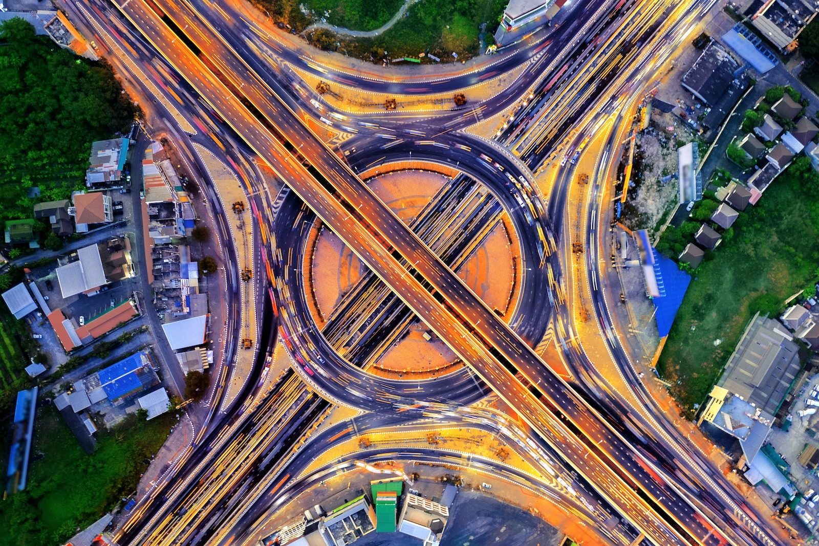 Aerial night view of a complex highway interchange with light trails from vehicles, centered around a large roundabout.